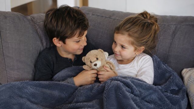 Siblings sharing comfort under a blanket on the sofa