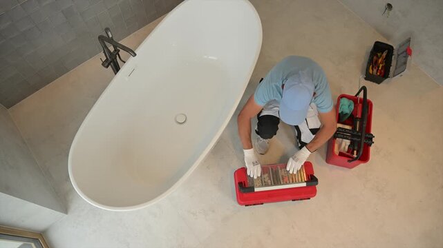 Worker opening a red toolbox beside a bathroom bathtub