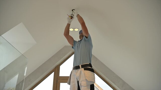 Worker servicing a ceiling fitting in a bright attic room