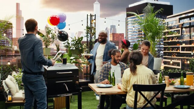 People laugh around an open rooftop barbecue grill as corn and patties cook, combining outdoor food preparation with friendly conversation and group bonding.