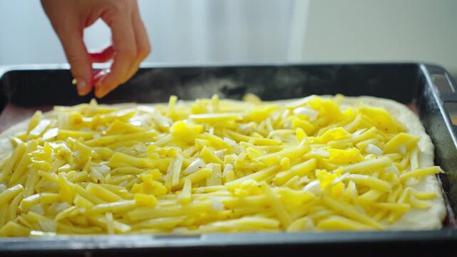 Hands sprinkle golden cheese over raw pizza dough. Cheese shreds fall with care, covering the flatbread evenly. Freshly prepared pizza, ready for baking, shown in close-up