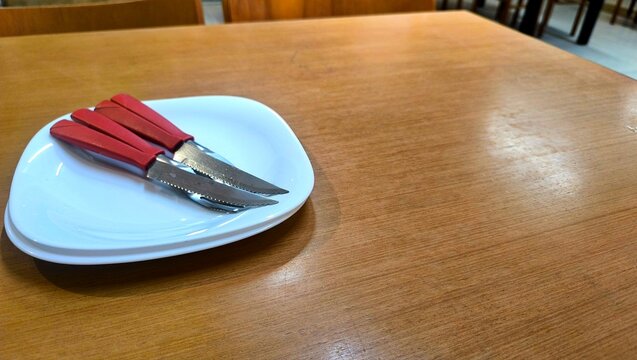 Set of red handles steak knives served on white plate