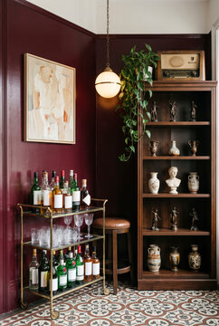 Nostalgic home bar corner with burgundy walls, brass bar cart, bottles and wooden display cabinet