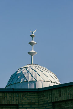 View of a white faceted dome with a tiered metal finial and crescent moon against a clear blue sky in Tashkent, Uzbekistan.