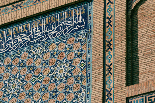 View of intricate blue and geometric tilework on a historic brick wall, featuring Arabic calligraphy and star patterns in Tashkent, Uzbekistan.