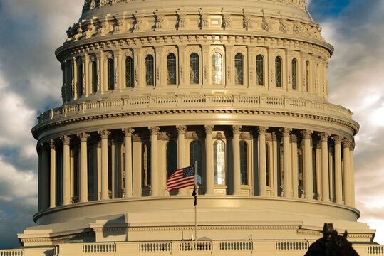 View of the United States Capitol dome with the American flag flying under a cloudy sky during golden hour in Washington, District of Columbia, United States.