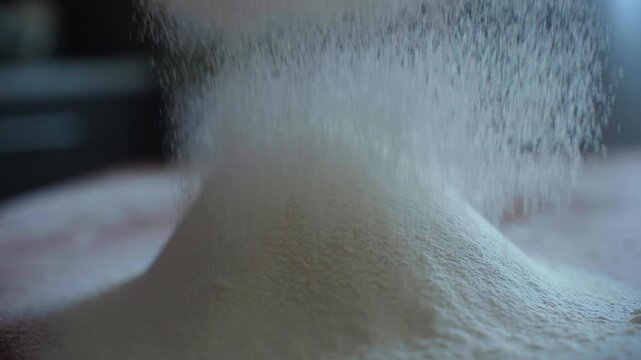 White powder pours onto a mound. Soft particles swirl in slow motion. Light catches the fine texture. Perfect for food or baking themes. Clean, crisp, and minimal visual. No people, no animals