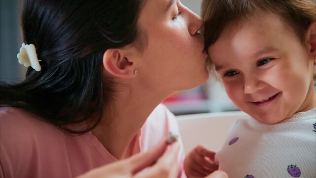 Soft kiss on a smiling child's cheek. Warm, tender moment between mother and baby. Joyful, affectionate interaction captured in close-up. Ideal for parenting, family, or emotional connection themes