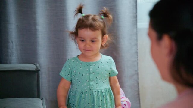 Little girl plays with doll near mother. Child smiles as she engages with toy. Mother watches with gentle affection. Playful moment at home. Ideal for family, parenting, or childhood themes