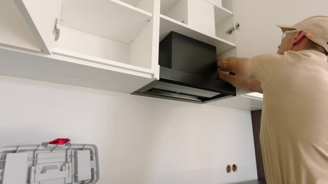 Installer adjusting an extractor hood between white cabinets