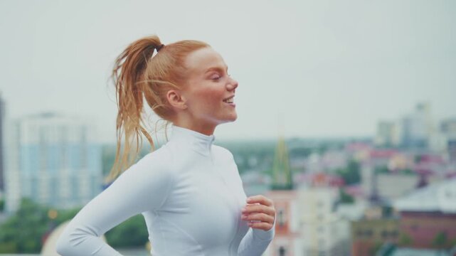 Young woman runs joyfully on rooftop. Her hair whips in the wind as she smiles. City skyline stretches behind her. Energetic and carefree, she moves forward. Perfect for health, wellness