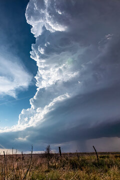 View of a massive supercell storm cloud looming over a vast, dry grassy field under a dramatic sky.