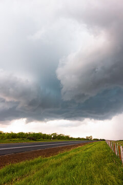 View of a dramatic storm cloud formation looming over a rural highway and green fields in Oklahoma City, Oklahoma, United States.