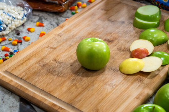 Green apple centered on wooden cutting board with sliced rounds and scattered candy pieces table top