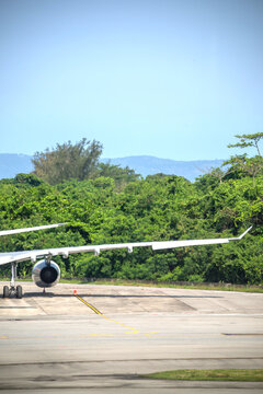 View of an airplane wing and engine on the tarmac at RIOgaleao International Airport, with trees in the background under a blue sky in Rio de Janeiro, Rio de Janeiro, Brazil.