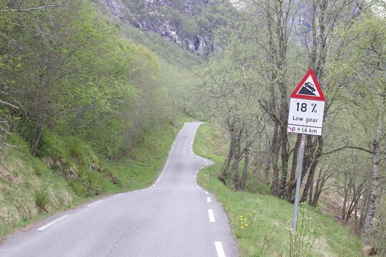 A winding mountain road through a dense forest with a sign indicating an 18 per cent gradient, Stalheimskleiva, Fjordland, Norway