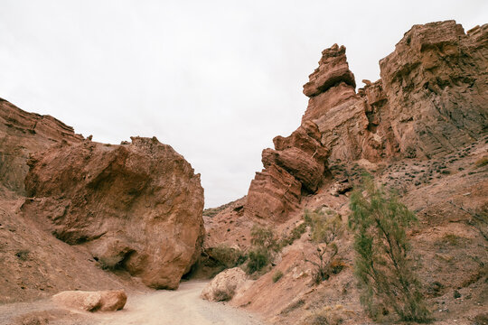 View of Charyn Canyon National Park with towering red sandstone rock formations and a narrow dirt path under a cloudy sky in Tamerlik, Almati oblisi, Kazakhstan.