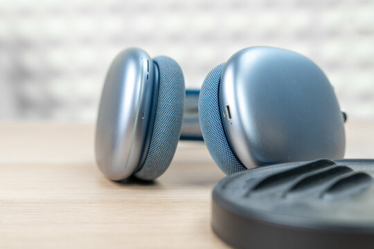 Blue wireless headphones with mesh ear cushions rest on a wooden table beside a black carrying case, a concept of private music and noise cancelling.