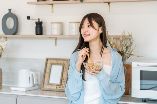 キッチンで手軽にグラノーラで朝食を取るアジア人女性