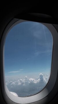 View through an airplane window showing blue sky, scattered clouds and distant patchwork land before the wing passes into dense white cloud cover