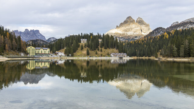 View of the Tre Cime di Lavaredo reflected in the calm waters of Lake Misurina, with pine forests and mountain hotels in Misurina, Belluno, Italy.