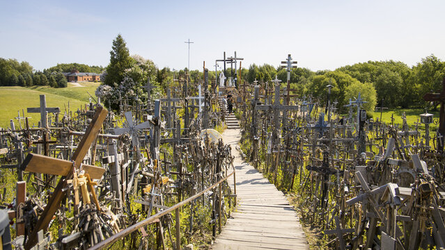View of the Hill of Crosses featuring thousands of crosses along a wooden path surrounded by green trees under a clear blue sky in Hill of Crosses, Siauliu apskritis, Lithuania.