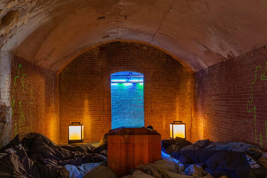 View of the interior of a historic brick casemate at Fort Pampus featuring a wooden structure, beanbags, lanterns, and neon light projections in Gooise Meren, North Holland, Netherlands.