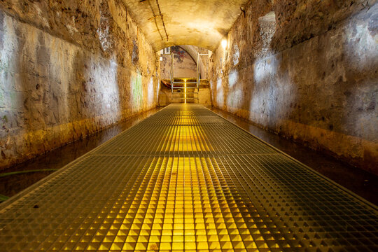 View of the illuminated underground tunnel with a metal grate walkway inside the historic Fort Pampus in Gooise Meren, North Holland, Netherlands.