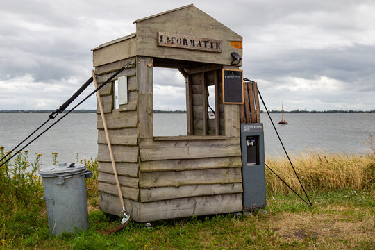 View of a rustic wooden information booth situated on the waterfront of Fort Island Pampus with a view of the water and a distant boat in Gooise Meren, North Holland, Netherlands.