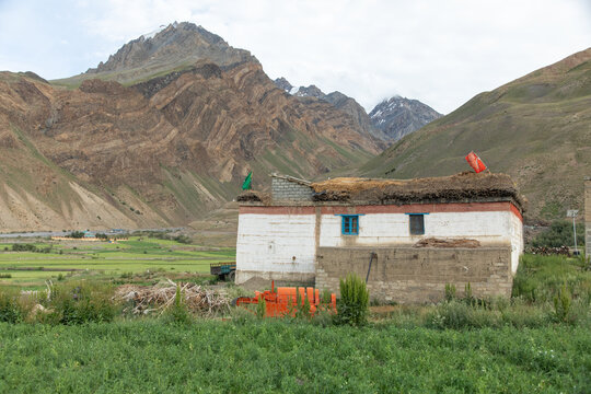 View of a traditional house with a flat roof and prayer flags in the Spiti Valley, set against the dramatic rugged mountains of the Himalayas in Kaza, Himachal Pradesh, India.