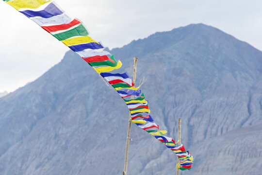 View of colorful Buddhist prayer flags fluttering in the wind against the backdrop of the rugged mountains in Nubra Valley, Diskit, Ladakh, India.