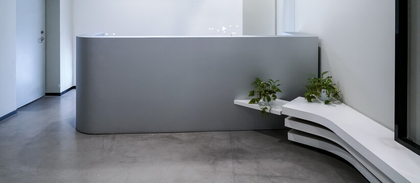 Minimalist grey curved reception desk with white layered bench and green pothos plants in modern office lobby
