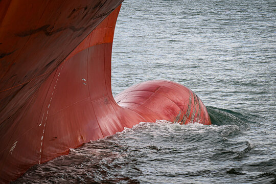 View of the red bulbous bow of a large cargo ship cutting through the water during shipping operations at Port of Tauranga, Tauranga, Bay of Plenty Region, New Zealand.