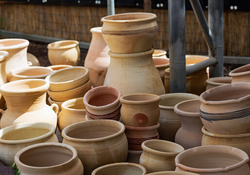 Stacked unglazed clay pots and jars of different shapes and sizes in beige and terracotta tones. Outdoor display of traditional pottery under natural sunlight. Flower pot for sale at the garden center