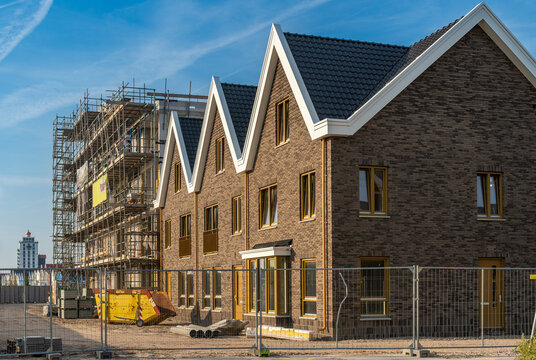 View of housing development with newly constructed brick houses next to a building site with scaffolding under a clear blue sky in Harderwijk, Gelderland, Netherlands