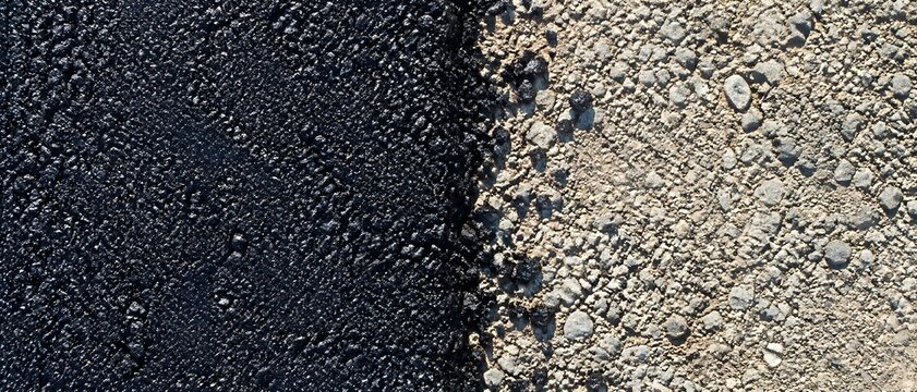 Distinct linear junction where new velvety black asphalt abuts a rough gravel highway subbase