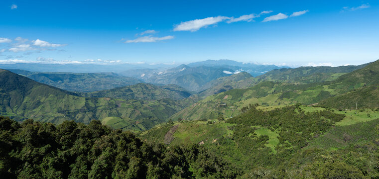 Vue panoramique de collines et de vall&eacute;es luxuriantes dans une r&eacute;gion montagneuse sous un ciel bleu.