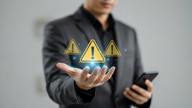 Businessman holding glowing yellow warning signs with exclamation marks above palm for digital security risk alert