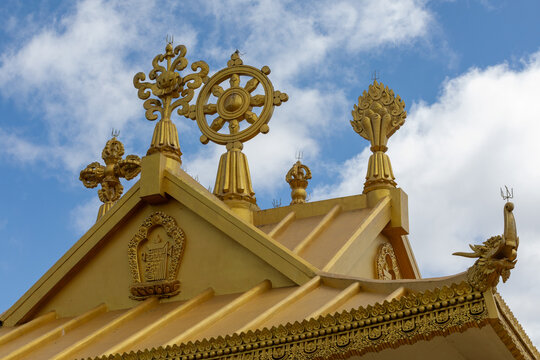 View of the golden roof ornaments of Namobuddha Monastery, featuring a dharma wheel and intricate Buddhist symbols against a blue sky with clouds in Simalchaur Syampati, Bagmati Province, Nepal.