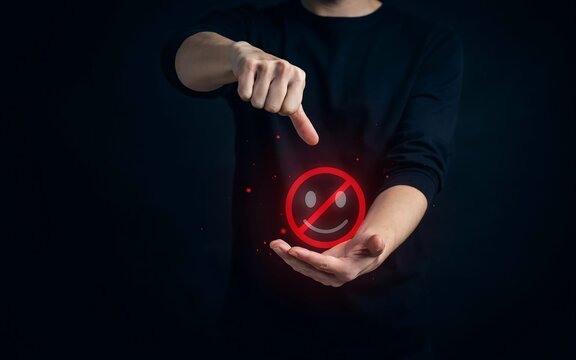 Person pointing at a glowing red forbidden smiley face icon held in their open palm against black