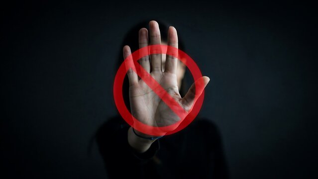 Person showing stop hand gesture with red prohibition sign overlay against a dark moody background studio shot
