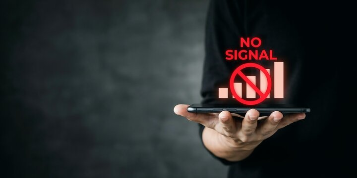 Person holding smartphone displaying no signal icon with red prohibition sign against dark textured background wall