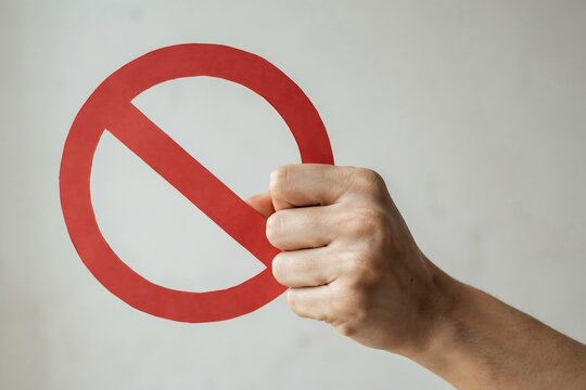 Hand holding a red circular prohibition sign against a plain white background for warning and restriction