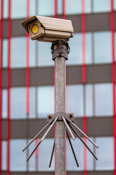 View of a security camera mounted on a metal pole with anti-bird spikes in front of the modern facade of the World Trade Center Almere, Almere, Flevoland, Netherlands.