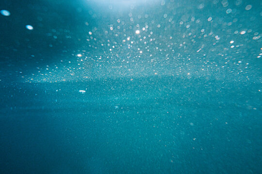 View of the clear blue water at Lulworth Cove with sunlight filtering through the surface and suspended particles in the United Kingdom.