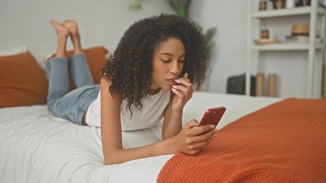 Woman lying on bed holding smartphone and biting fingernail in a studio setting; pensive introspection.