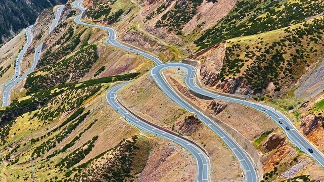 Winding asphalt highway curves through steep mountain slopes along Duku Highway in Xinjiang, captured from a high angle.