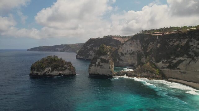 Drone footage captures the dramatic limestone cliffs and turquoise waters of Diamond Beach on Nusa Penida. Crisp daylight, blue sky, and vibrant, foamy waves highlight this tropical paradise.