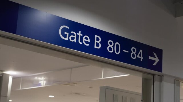 Overhead wayfinding board reading Gate B 80 to 84 in a terminal corridor, pointing passengers toward boarding.