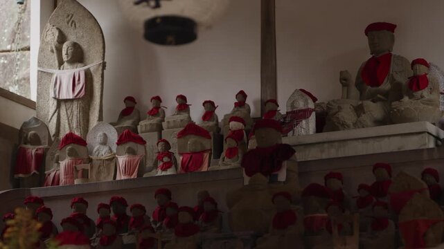 Stone Buddhist figures of Ojizo sama, guardians of children and travelers, dressed in knitted hats and aprons on tiered shelves inside a hall in Japan.